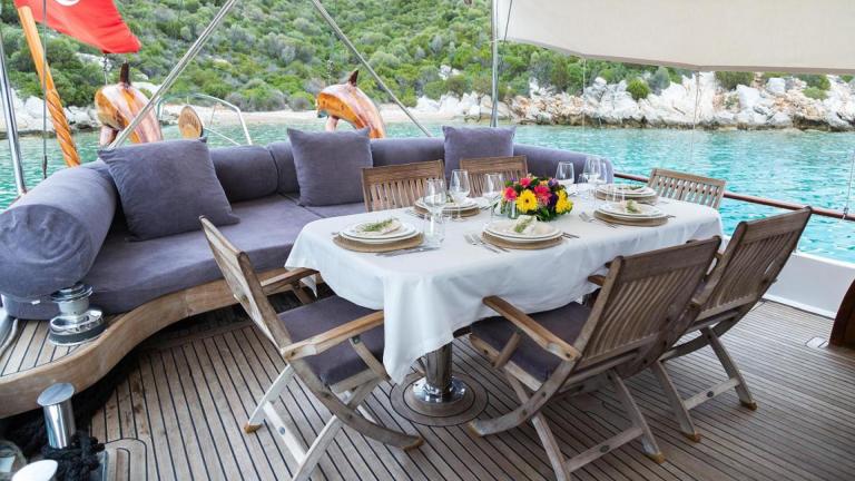 Served table decorated with fresh flowers and a sofa at the stern of the gulet